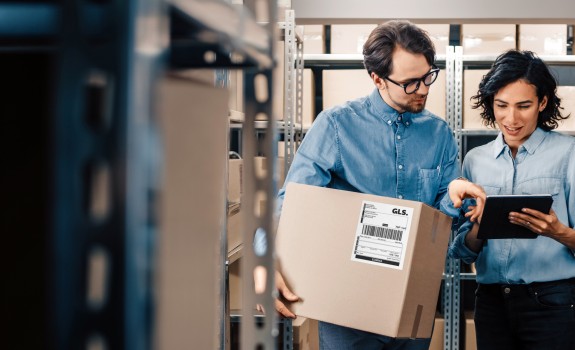 Two people in a warehouse with a box looking at a tablet